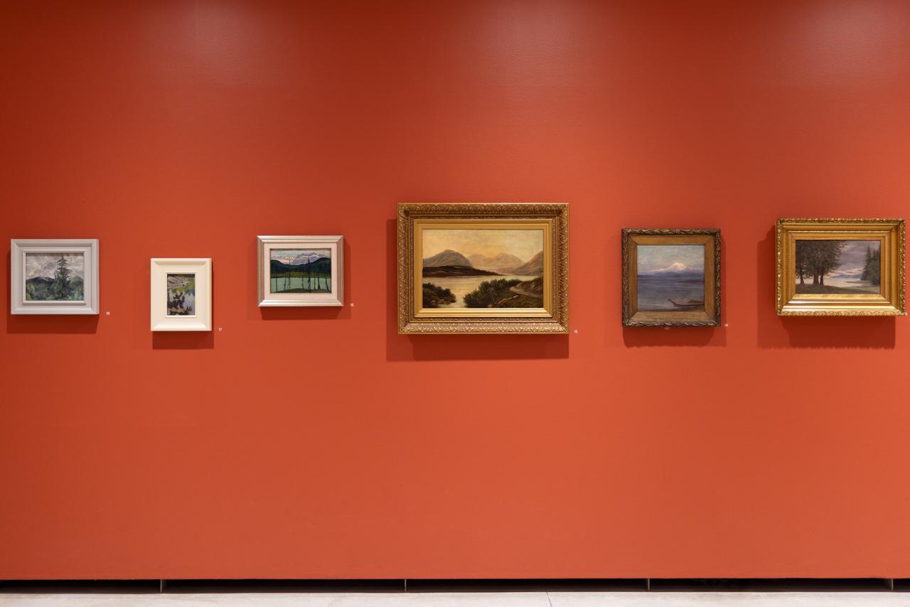 Six landscape paintings are hung against a vermillion wall. The frames are shifted up and down on the wall in order to align the horizon lines of each different forest setting. 