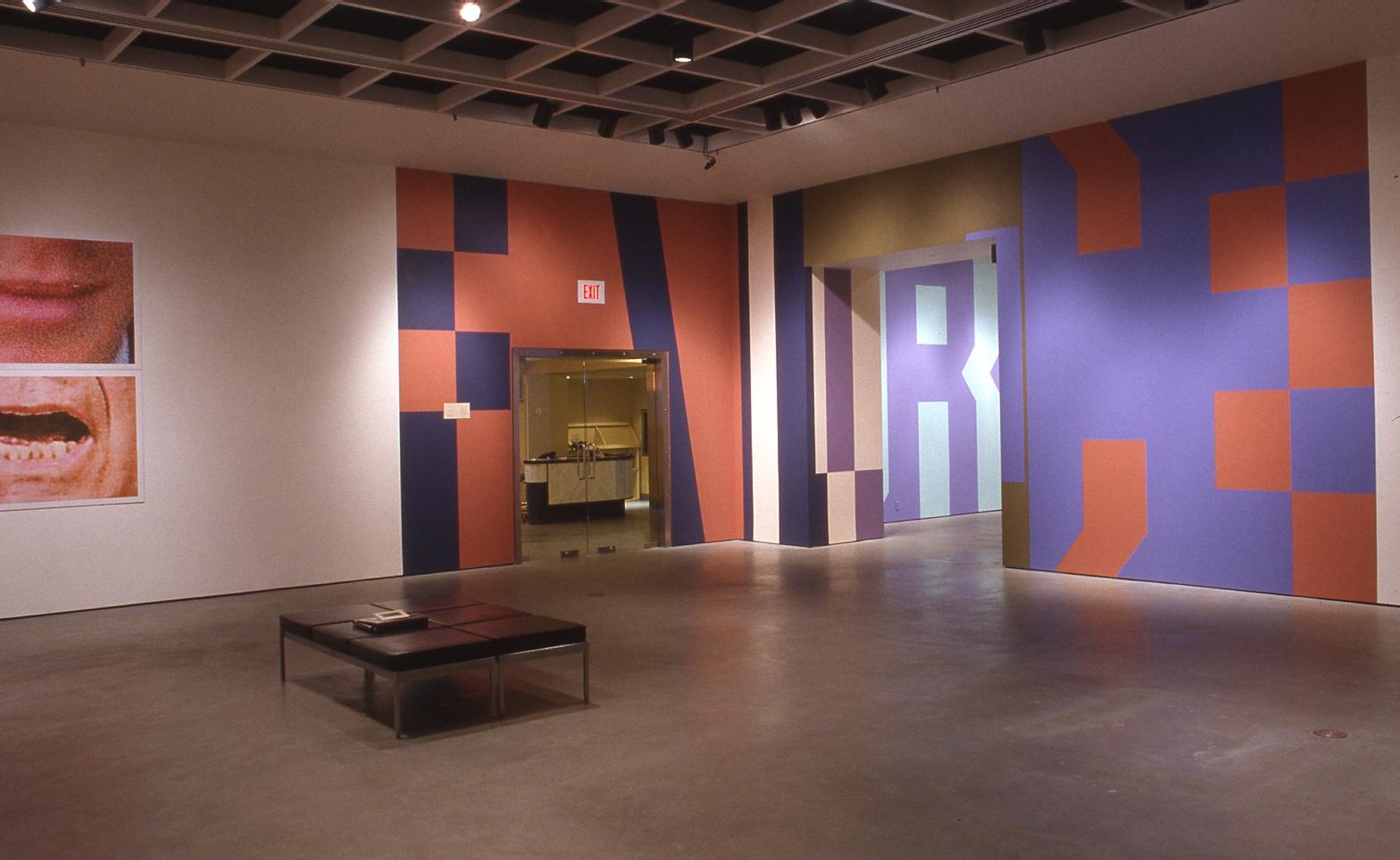 Large block letters in Superstar Shadow font stretch from floor to ceiling as they slink around a glass door and into the back gallery. F,A,I,L, part of an R and an E can be seen wrapping around the walls in navy blue, rusty orange, purple and lilac. The rest of the gallery is open with a small black bench in the centre and two partial, closely cropped images of mouths midway through speaking hang of the far left. 