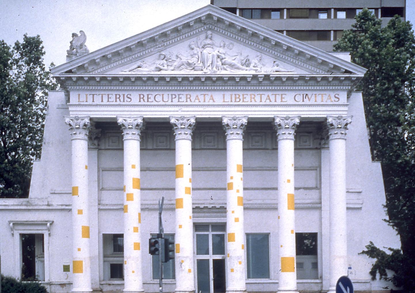The corinthian columns of a white Grecean style building are scattered with yellow squares of various sizes.