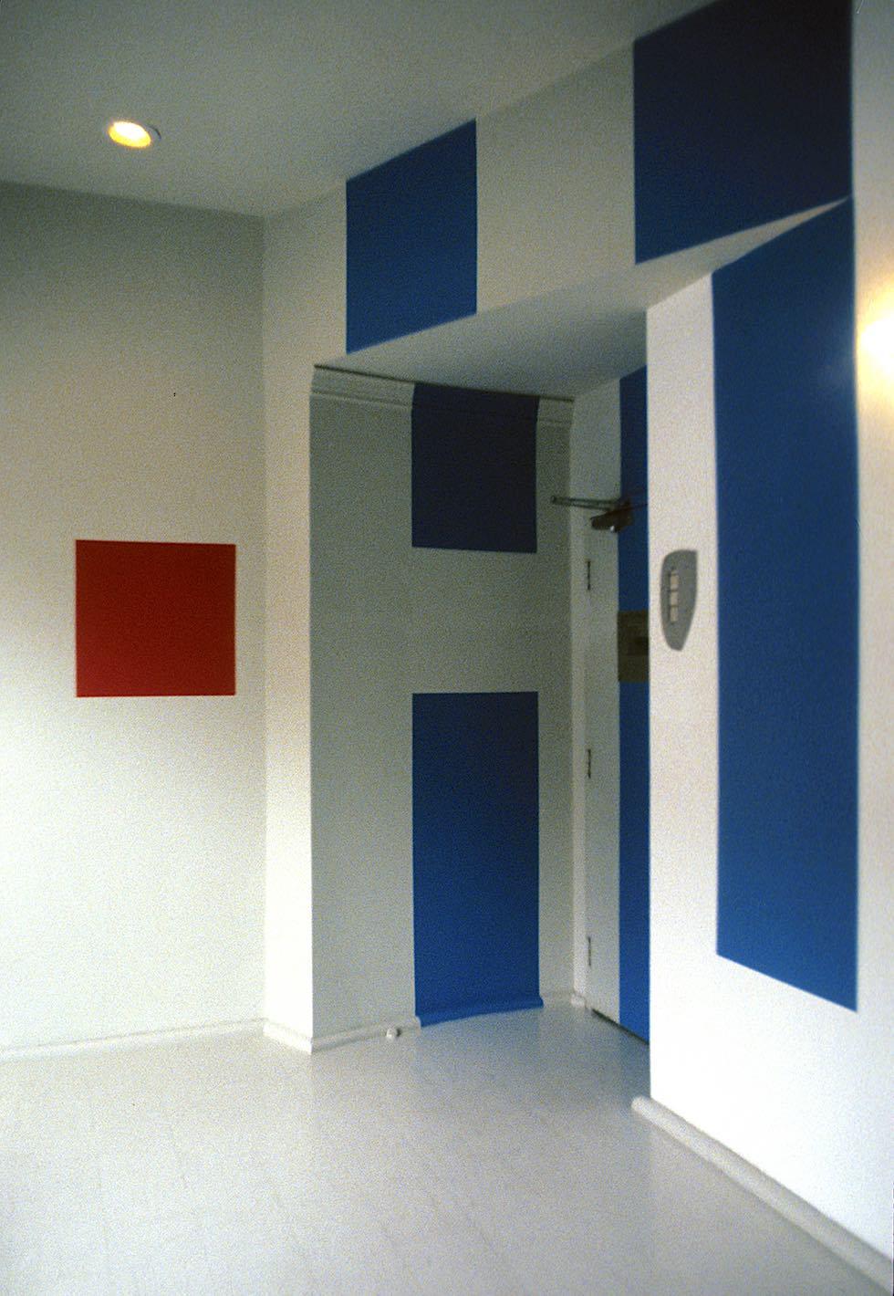 A red square painted high up on the wall of a gallery space bridges large blue and white lettering painted on the wall in Superstar Shadow font. An H and a U can just be made out as the large letters stretch from floor to ceiling and wrap around the room.