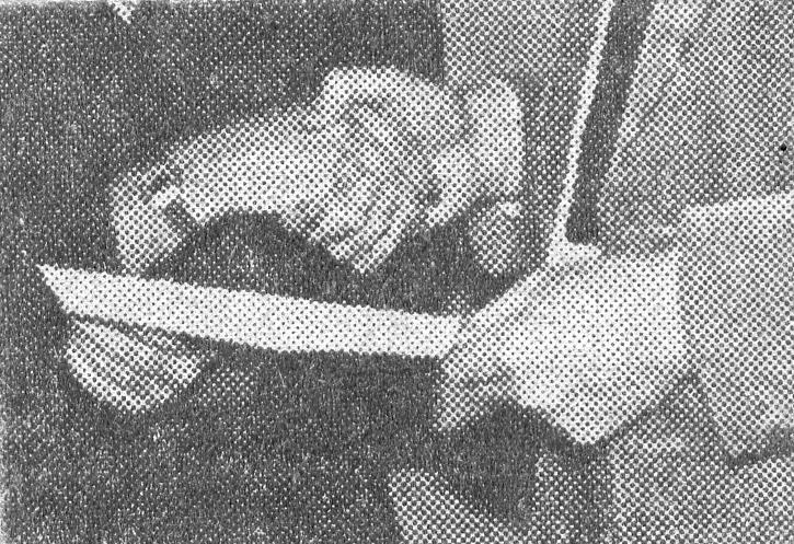  A close up of a half-tone newspaper photograph of two people shaking hands while exchanging a slip of paper. The image is cropped to only show the body's hands and waists. The person on the left wears a dark suit and a watch and the person on the right is in a light suit with a white shirt and black tie.
